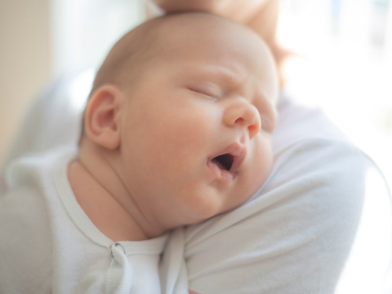 Unrecognizable mother holding her sleeping newborn boy on her shoulder.