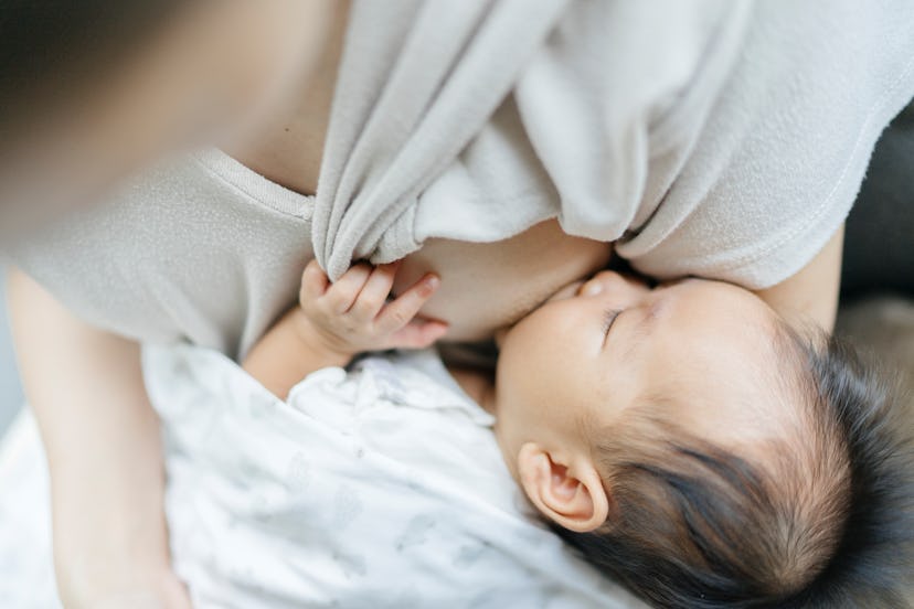 Baby grapsing onto mom's breast while breastfeeding, demonstrating why having hands free rather than...