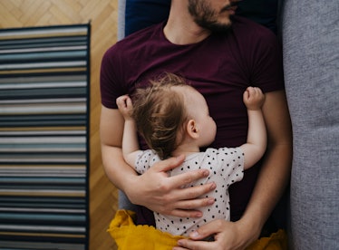 A dad sleeps on a couch with his baby on his chest.