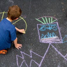 A boy draws with chalk in the driveway of his home.