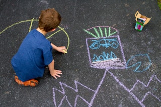 A boy draws with chalk in the driveway of his home.