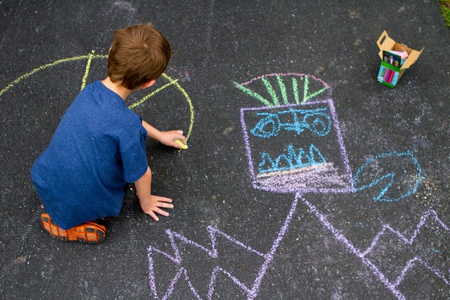 A boy draws with chalk in the driveway of his home.