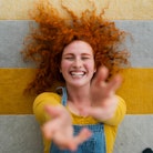 cheerful young woman with red hair playfully reaches toward camera as she thinks about the spiritual...