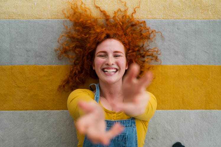 cheerful young woman with red hair playfully reaches toward camera as she thinks about the spiritual...