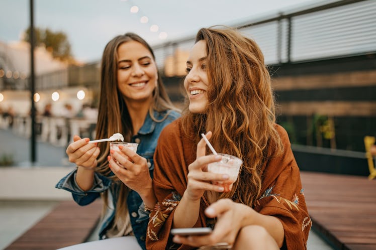 Two young women enjoy frozen drinks as they discuss the summer 2022 solstice, which will affect thei...