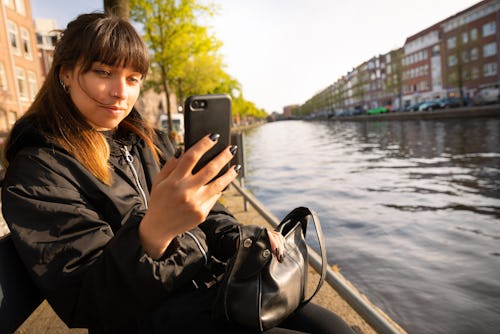 Young woman using smartphone outdoors. Here's how to use instagram reels templates
