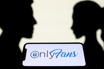OnlyFans logo displayed on a phone screen is seen with paper silhouettes looking like a man and a wo...