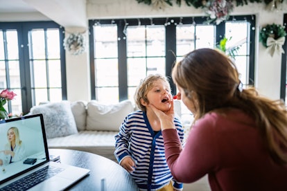 Mother using a throat swab Covid test on her child at home during a video call with a doctor.