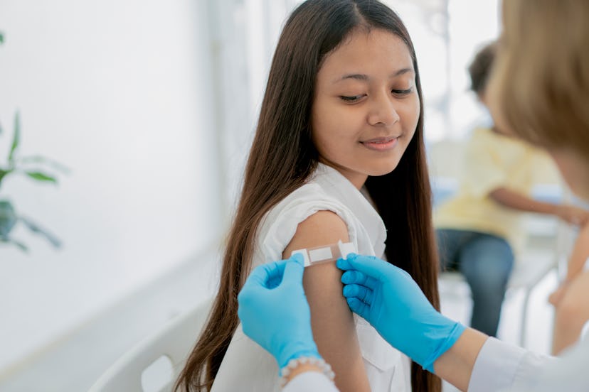 A doctor applies a bandage to a girl's upper arm when getting a booster after Covid infection.