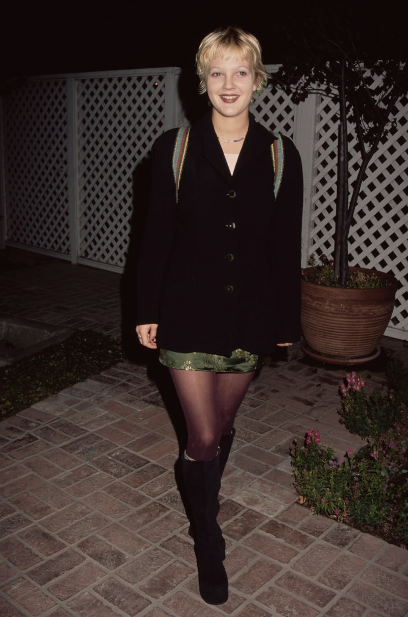 American actress Drew Barrymore, wearing a black jacket over a green miniskirt, with what are possib...