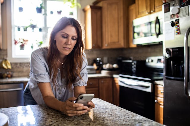 Woman using mobile device in kitchen at home