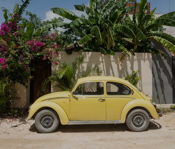 In Tulum, Mexico a vintage, yellow Volkswagen Beetle is parked outside on a residential street on a ...