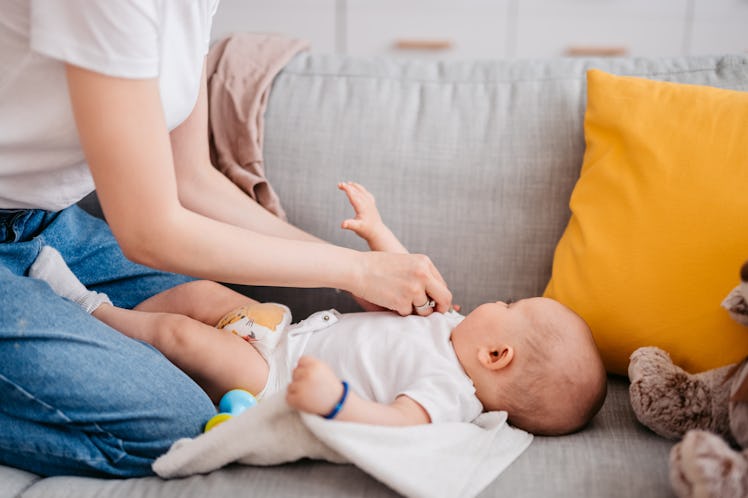 Young mother changing her baby boy's diaper on the sofa.