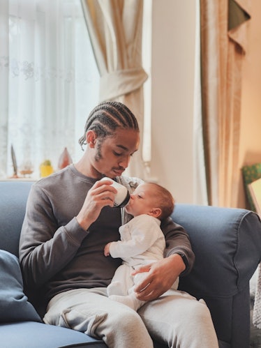 A dad on a couch feeding his baby with a baby bottle.