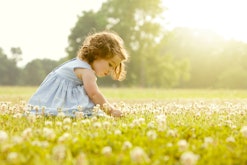 a little girl in a sunny flower meadow in an article about baby girl names that start with "M"