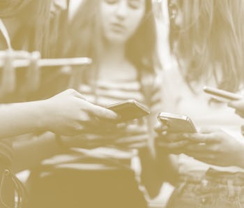 Group of teenage students standing in schoolyard and using mobile phones. They are very happy and pl...