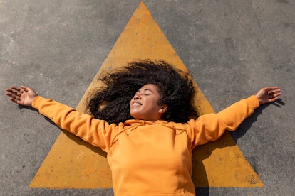 Young woman lays out on a yellow triangle as she thinks about the spiritual meaning of the July 2022...
