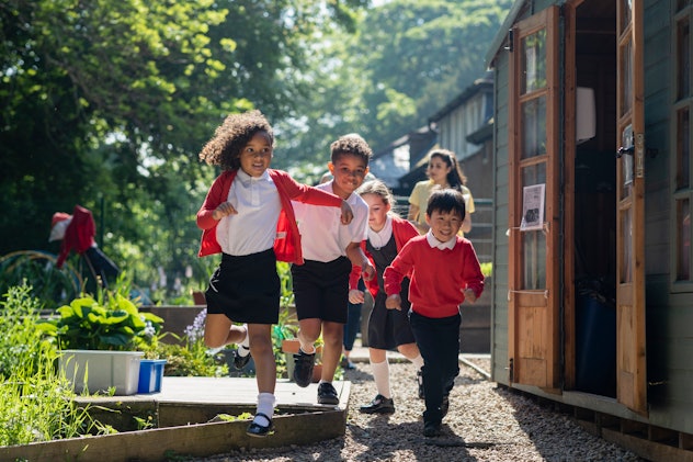 A medium close-up of a group of school children running in the school yard wearing red in an article...