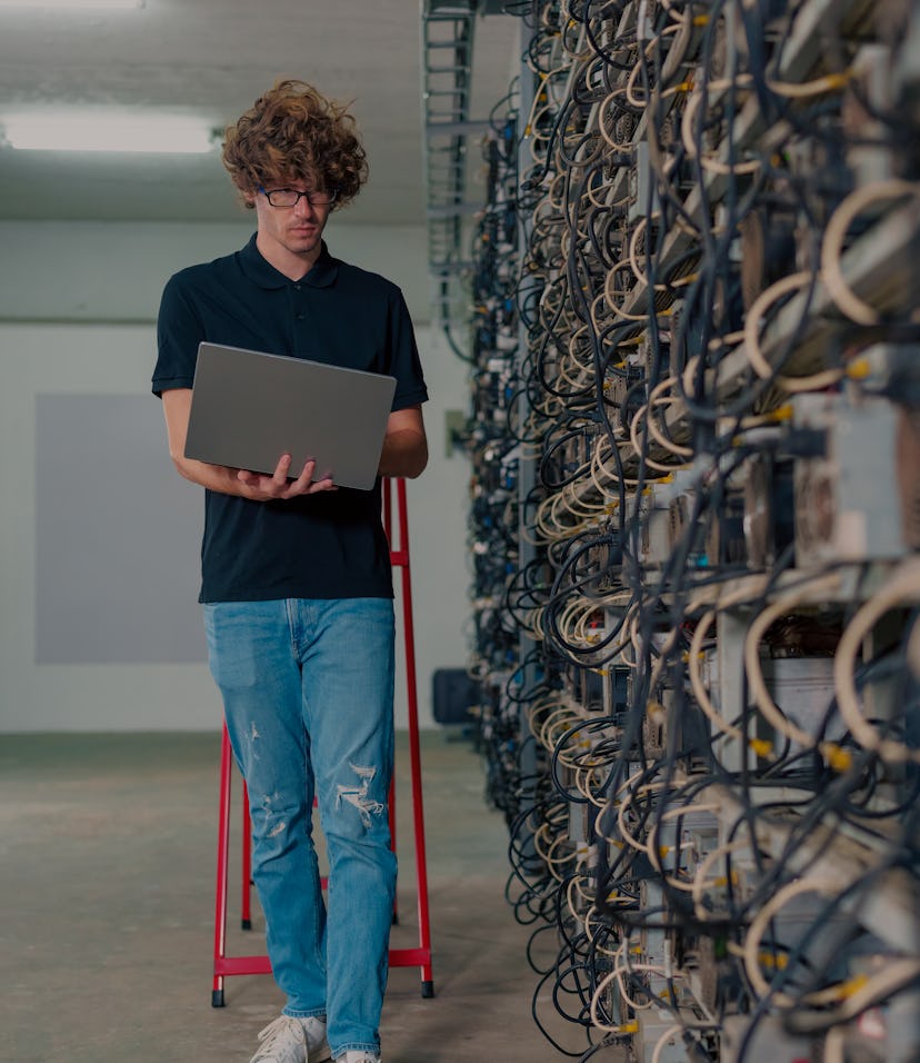 Professional engineers carrying the laptop working in crypto mine. Crypto mine management software. ...