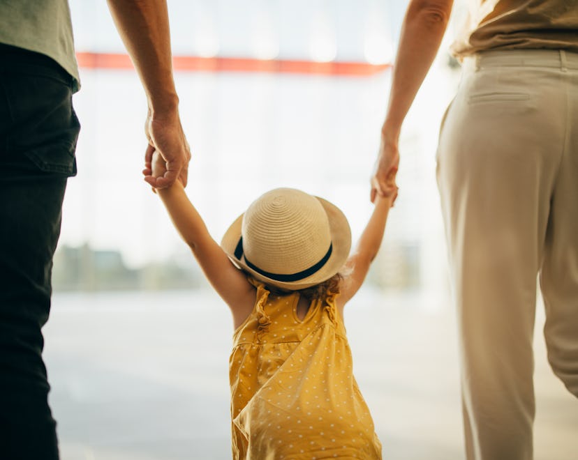 Close up photo of anonymous parents holding hands of their little girl at the airport