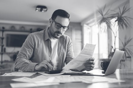 Young man using calculator while working on his financial plans at home.