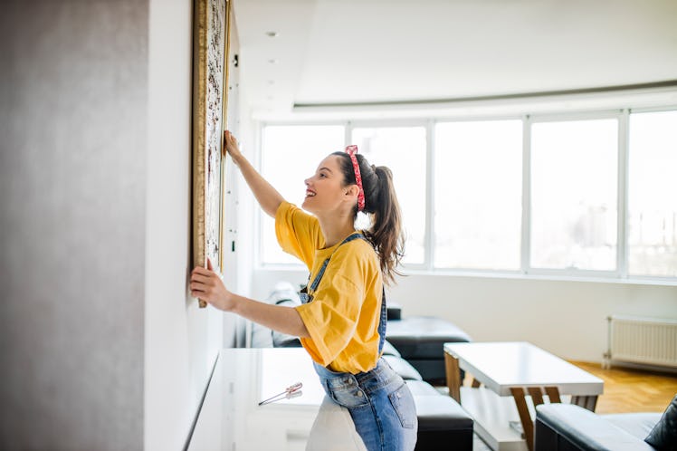 Young woman hanging a picture on a wall as a DIY project uses it as one of her Instagram reel ideas.