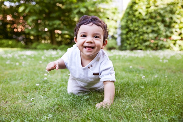 baby boy crawling and smiling in a daisy meadow, in an article about baby boy names that start with ...