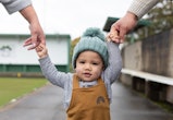 baby boy walking with parents and holding their hands in an article about baby boy names that start ...