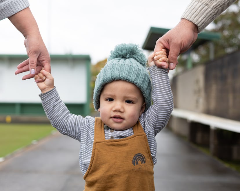 baby boy walking with parents and holding their hands in an article about baby boy names that start ...