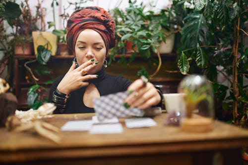 Female fortune teller smoking rolled cigarette while laying out divination cards. These are the four...