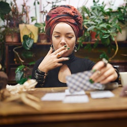 Female fortune teller smoking rolled cigarette while laying out divination cards. These are the four...