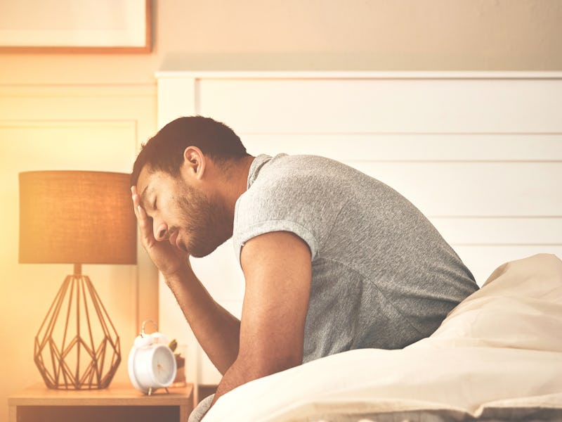 A depressed and sad man suffering from insomnia sitting on a bed at home in the morning. Tired and e...