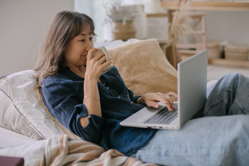 A woman drinks coffee on her laptop. Here’s your July 15 zodiac sign daily horoscope