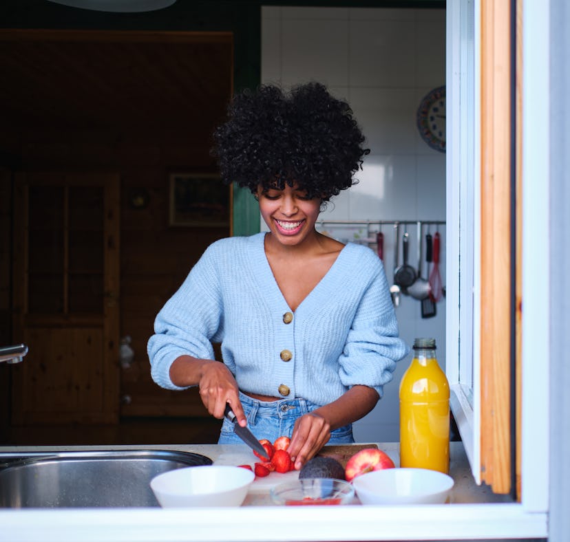 front view of young latina woman cutting fresh fruit in kitchen for how to make the viral deviled st...