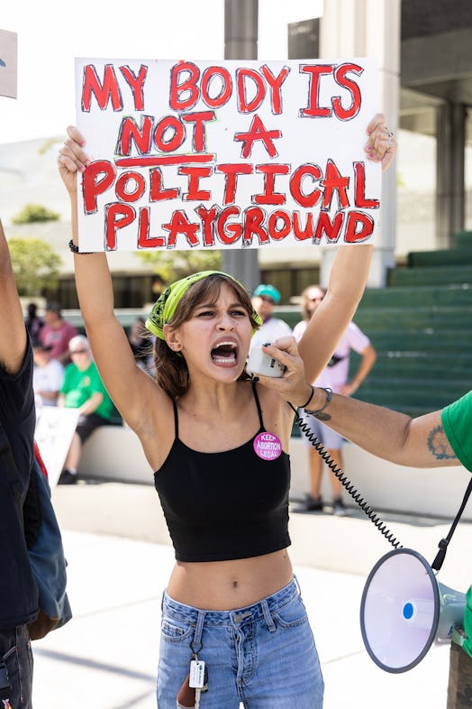 A woman holding a "my body is not a political playground" banner and protesting to support abortion ...