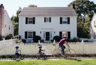 Father and twin 4-year-old sons riding bicycles in front of suburban home