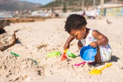 Cute black girl playing with a sand pail and shovel during a sunny day at the beach in summer, best ...
