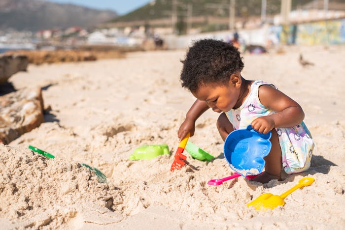 Cute black girl playing with a sand pail and shovel during a sunny day at the beach in summer, best ...
