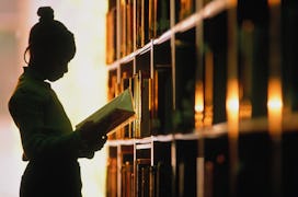 a girl reads a book in a library in an article about the sight words for first grade, words that fir...