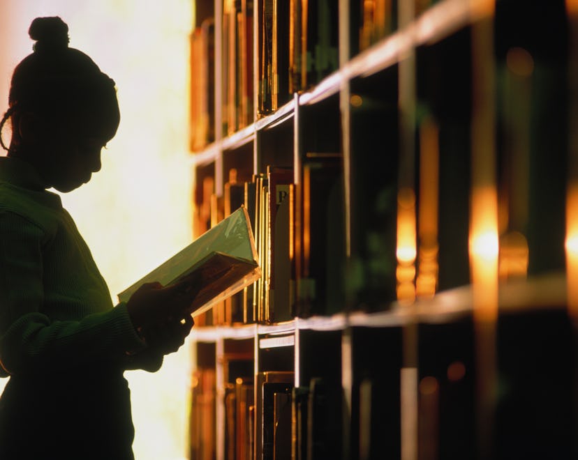 a girl reads a book in a library in an article about the sight words for first grade, words that fir...