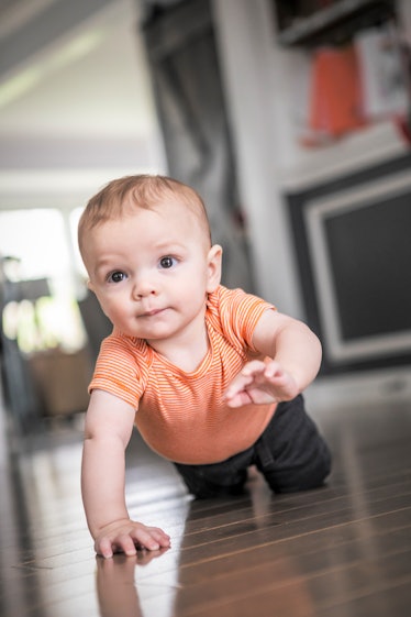 An 8 month old baby boy crawling across the hardwood floors of his home.