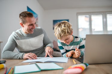 Waist up shot of proud single white father pointing answers on the notebook to little son. They are ...