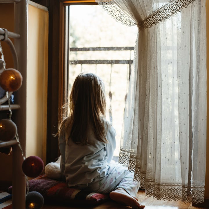 A lonely child stares out the window — new research links childhood loneliness to problem-drinking a...