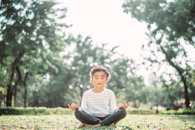 A ittle girl in closed eyes sitting with crossed legs while practicing yoga, mindfulness activities ...