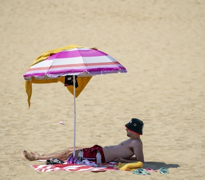 A man shelters under a umbrella on the beach in Bournemouth. Britons are set to melt on the hottest ...