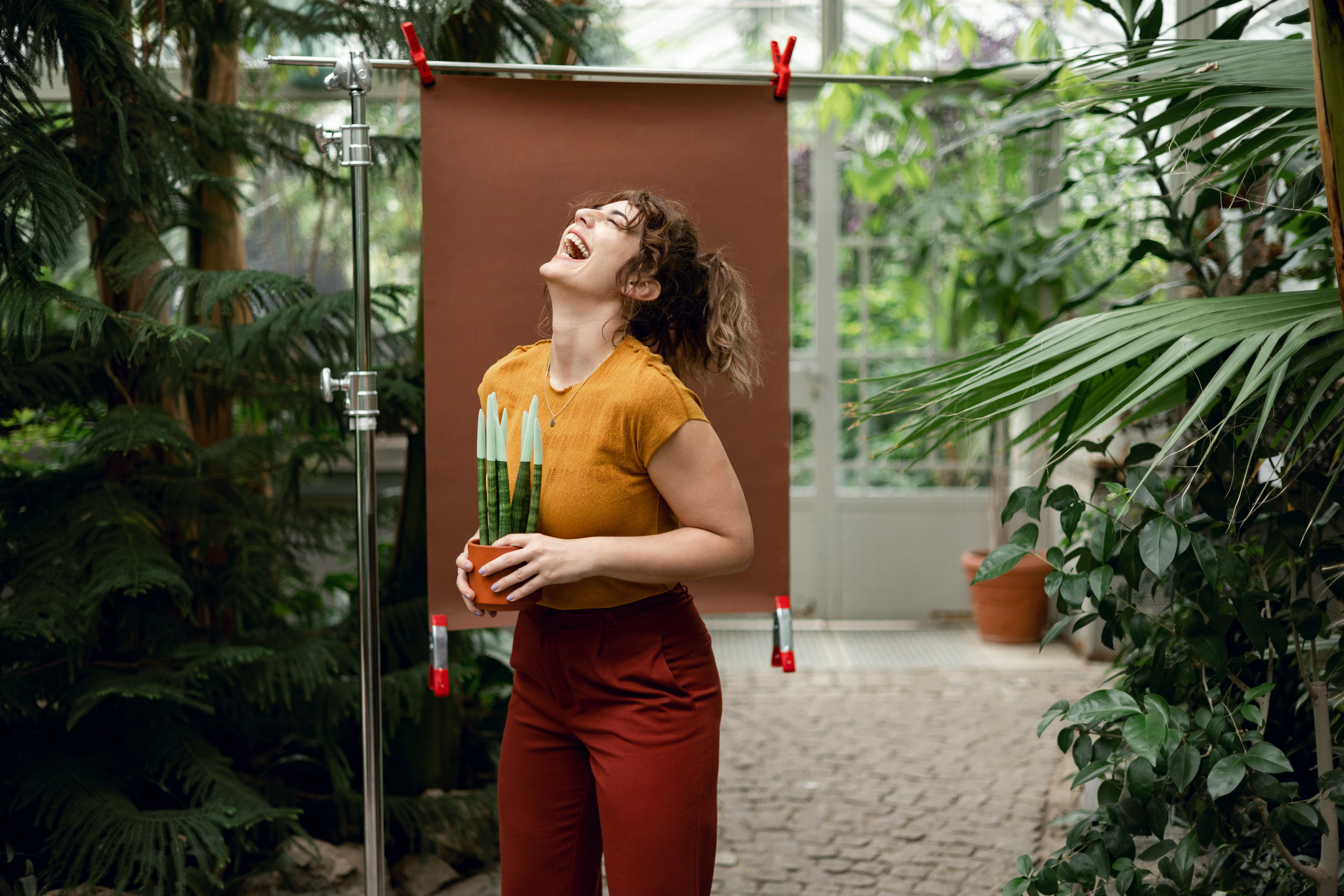 Cheerful woman standing in a botanical garden with a brown colour backdrop setup behind her holding ...