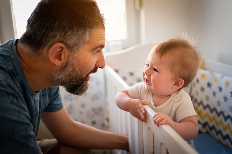 Side view of curious Caucasian baby boy in the crib, and his father