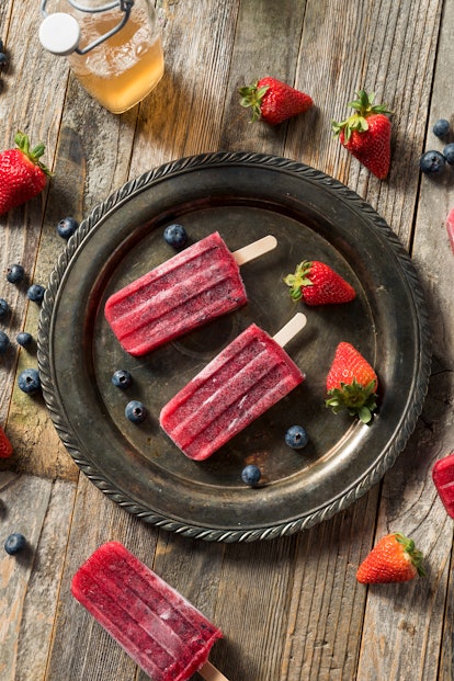 Homemade frozen fruit popsicles on a plate with strawberries and blueberries for summer popsicle ins...
