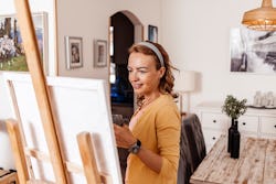 A woman paints a canvas at home. Here's your july 22 zodiac sign daily horoscope.