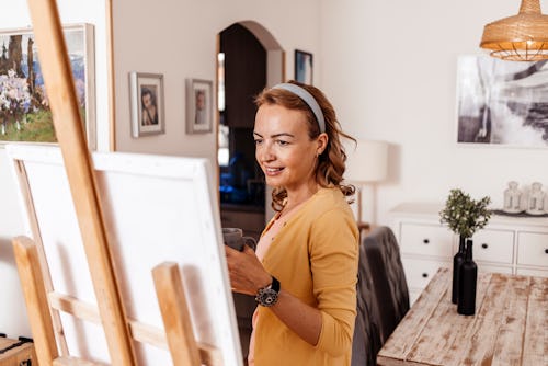 A woman paints a canvas at home. Here’s your july 22 zodiac sign daily horoscope.